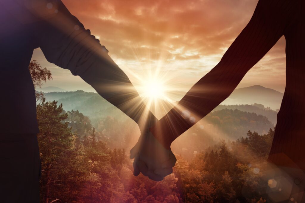 A close-up of two people's hands holding each other, as they face a beautiful valley at sunrise.